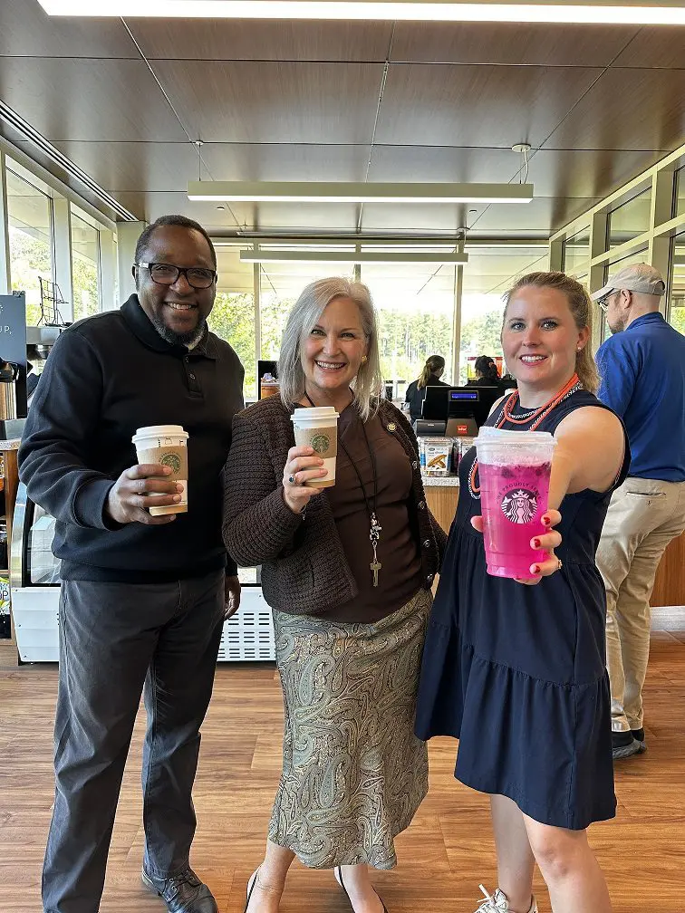 Three people holding up Starbucks drinks